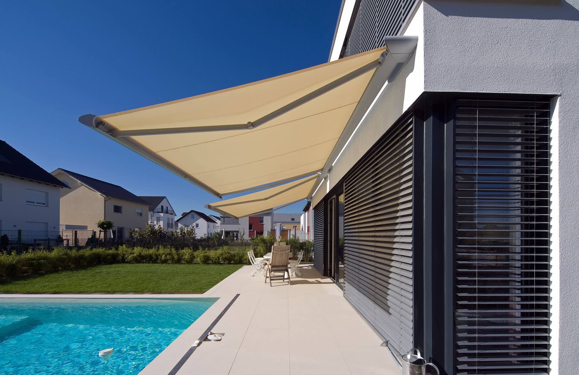 Weit ausgefahrene Gelenkarmmarkise über einer Terrasse mit Pool
