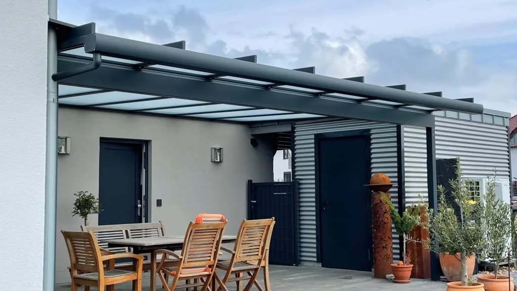 Dunkle Aluminiumkonstruktion mit transparenter Glaseindeckung über einer Terrasse